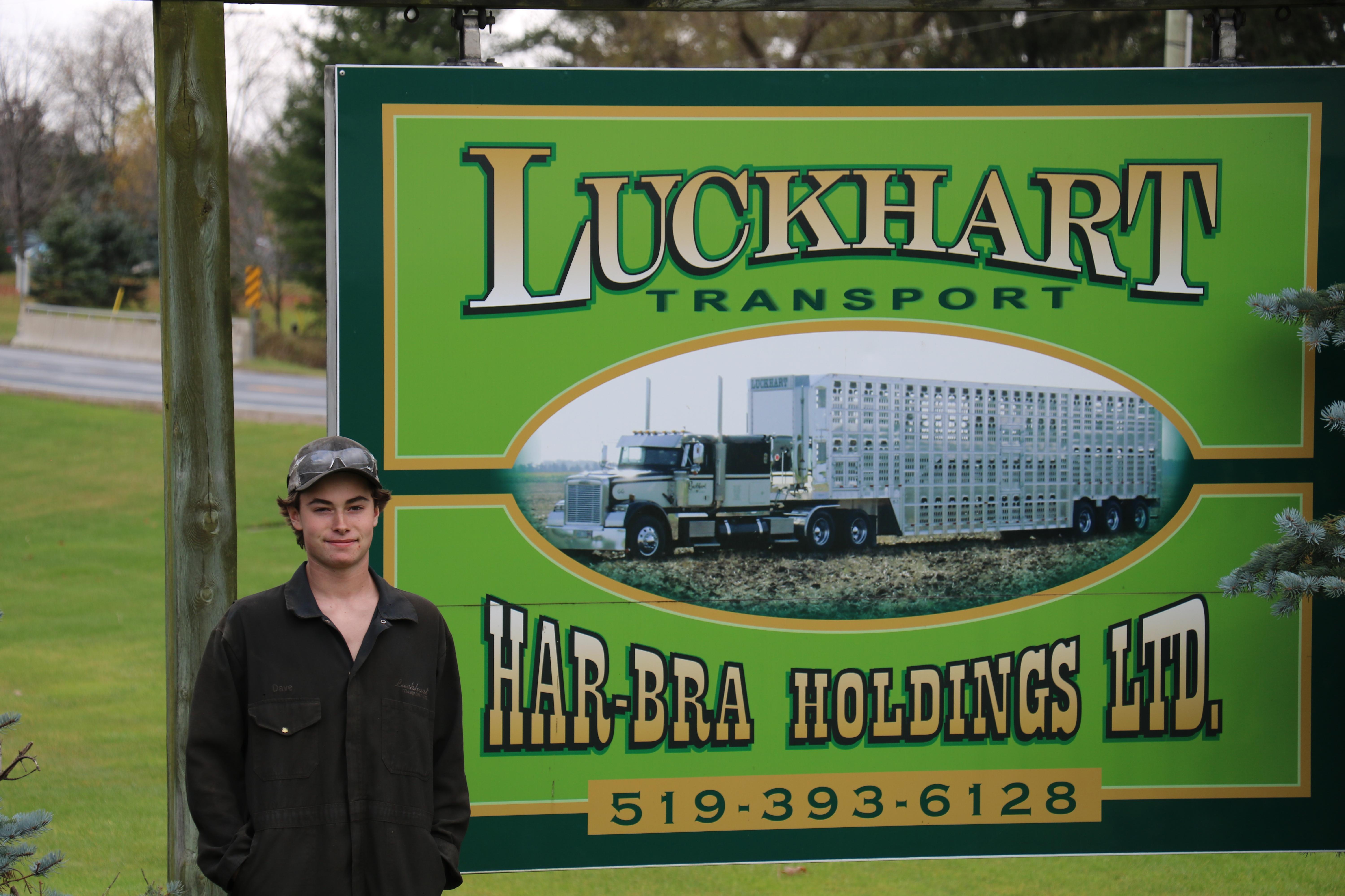 student standing in front of sign which says Luckart Transport