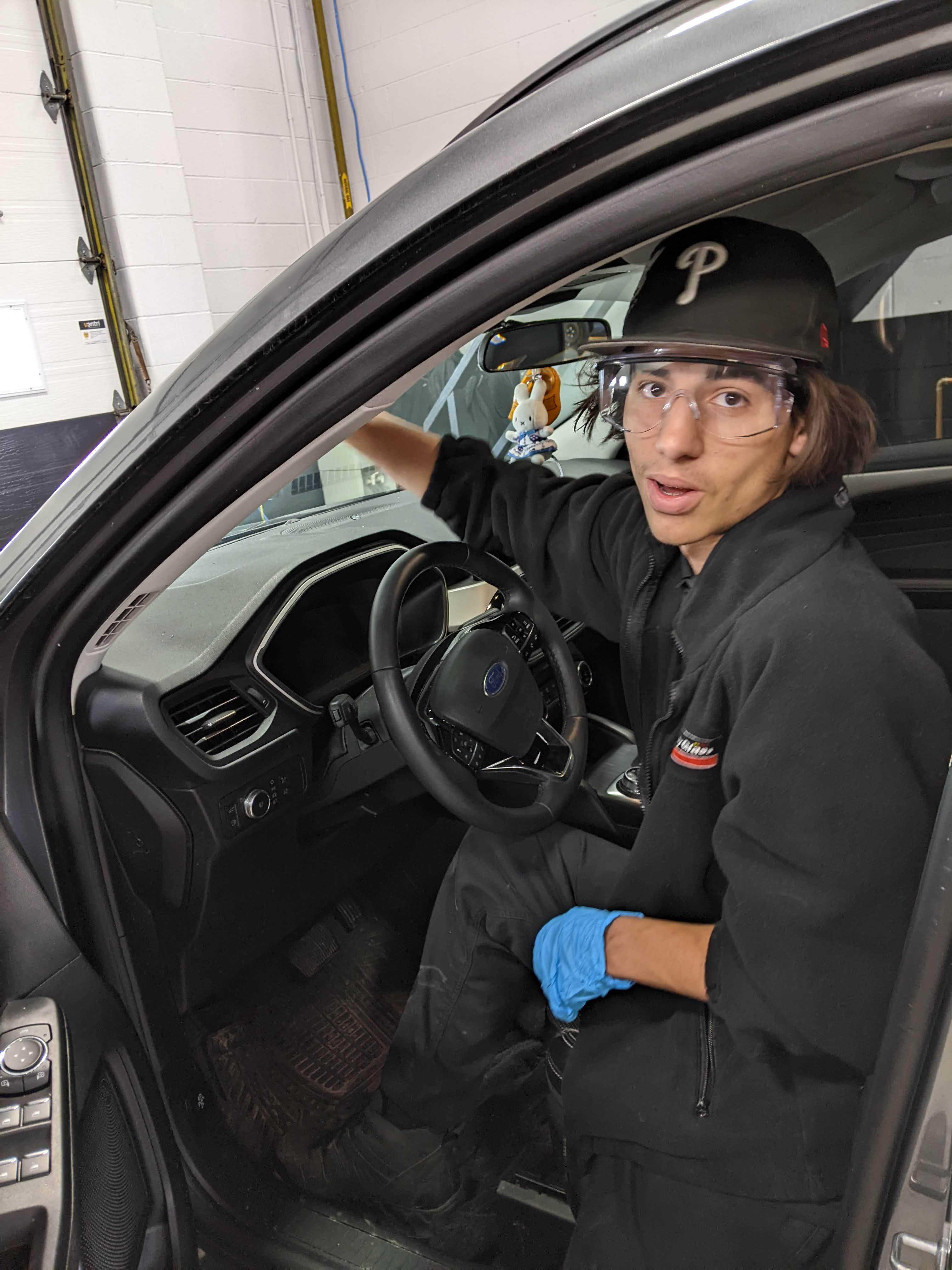 student sitting in car at work in a garage